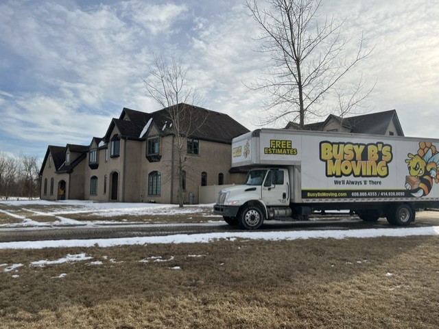 Busy B’s Moving branded truck parked beside a house with snow on the lawn